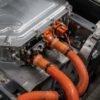 Orange high voltage cables connected to an EV inverter housing on the vehicle floorpan with orange high voltage connectors and braided sleeving