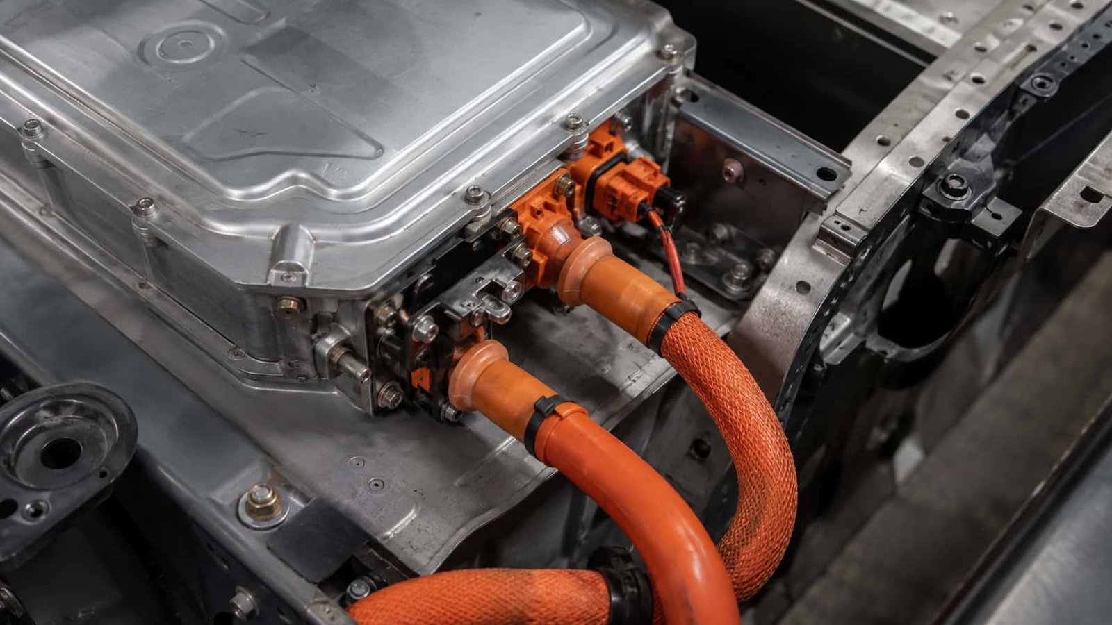 Orange high voltage cables connected to an EV inverter housing on the vehicle floorpan with orange high voltage connectors and braided sleeving