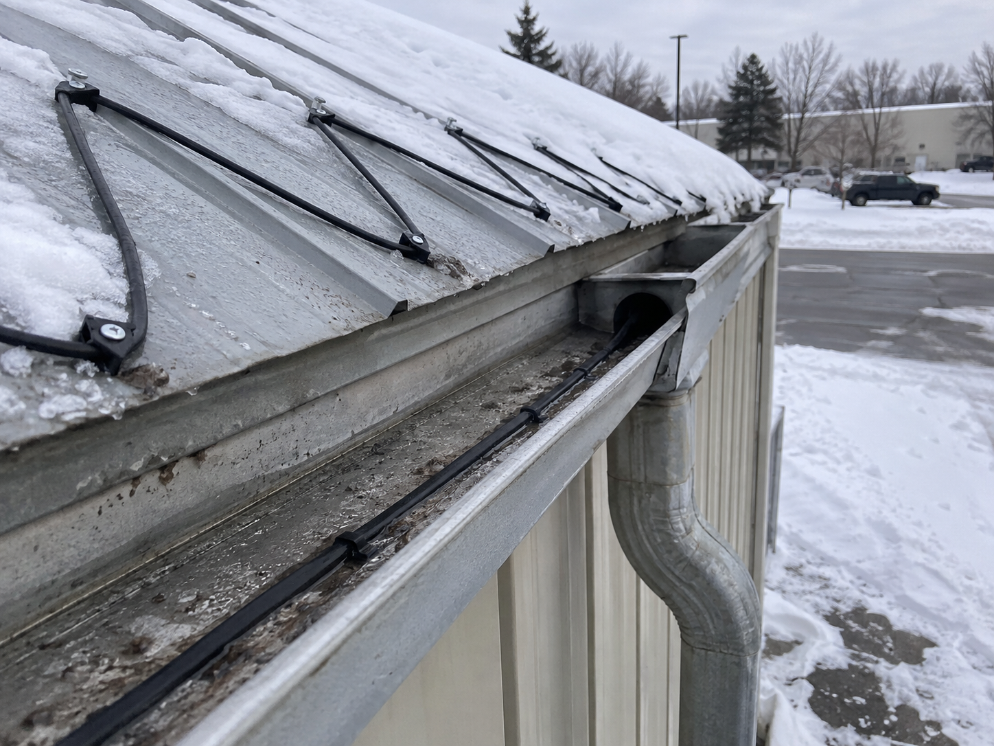 Self-regulating heat trace cable routed through a roof gutter and downspout for ice prevention
