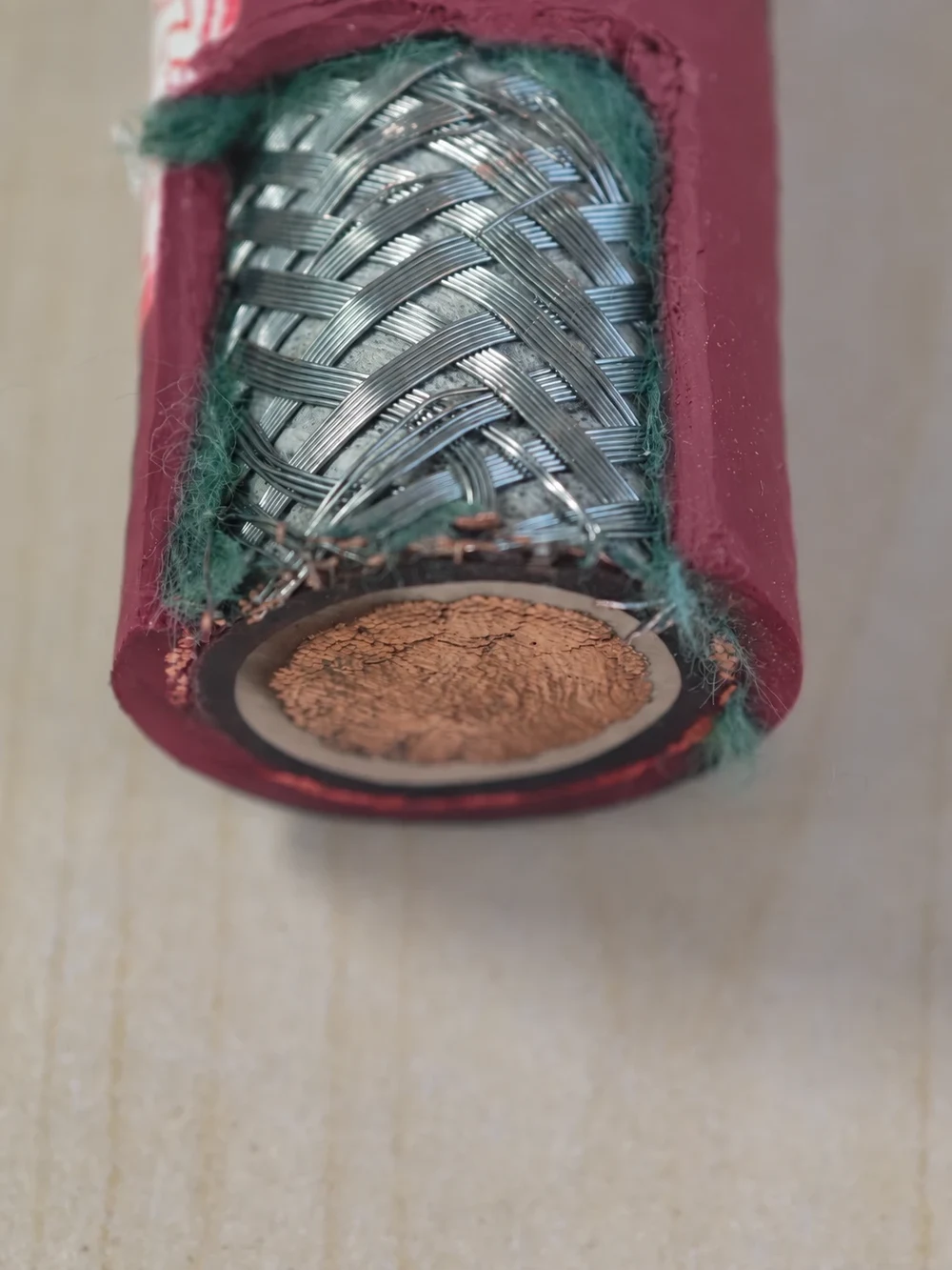Tinned copper braided shield exposed on a red-sheathed cable sample, showing carriers of wires crossing over and under