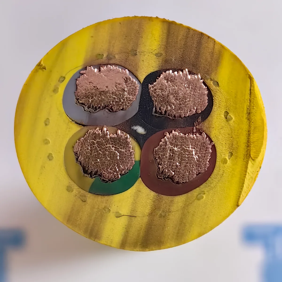 Extrémité d'un câble enrouleur de grue jaune (N)SHTÖU 4 × 16 provenant d'une commande TEBAOFLEX, montrant quatre conducteurs en cuivre en isolant vert-jaune, marron, noir et gris et la tresse anti-torsion sous forme d'anneau de fils fins à l'intérieur de la gaine
