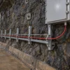 Cabo alimentador mineiro vermelho, armado e fixo, preso a uma escada de cabos em túnel e ligado a um quadro de distribuição fechado