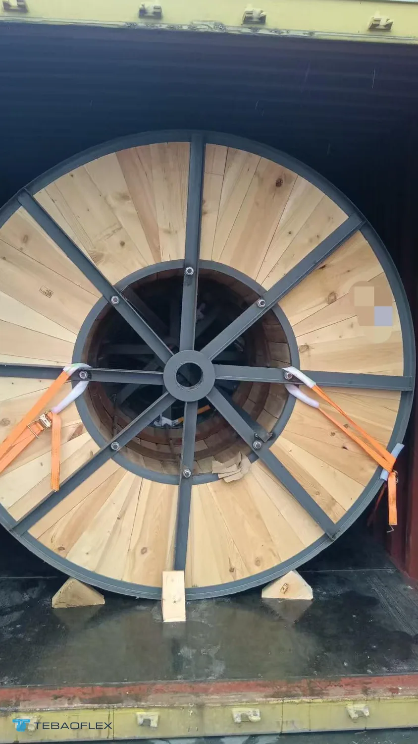 Un touret de câble posé sur des cales en bois à l'intérieur d'un conteneur de 20 ft, sanglé aux parois latérales
