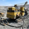Hochspannungs-Tagebau-Schleppleitung UGF & UGEFP (3.6/6–6/10 kV) — Anwendungsszene Tagebaustrosse mit einem großen elektrischen Seilbagger, der über eine auf einer Kabelkufe geführte schwere schwarze runde UGF-Hochspannungs-Schleppleitung versorgt wird